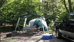 A camping setup with a tent, a table, chairs, and a cooler. - Tent and Tear Drop Electric site 10 (Wellsboro)