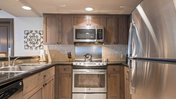 A modern kitchen with stainless steel appliances, wooden cabinets, and a tiled backsplash. - Saint James Place 210 (Beaver Creek)