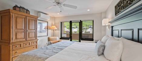 A bedroom with a large bed, wooden wardrobe, ceiling fan, and a view of greenery outside.