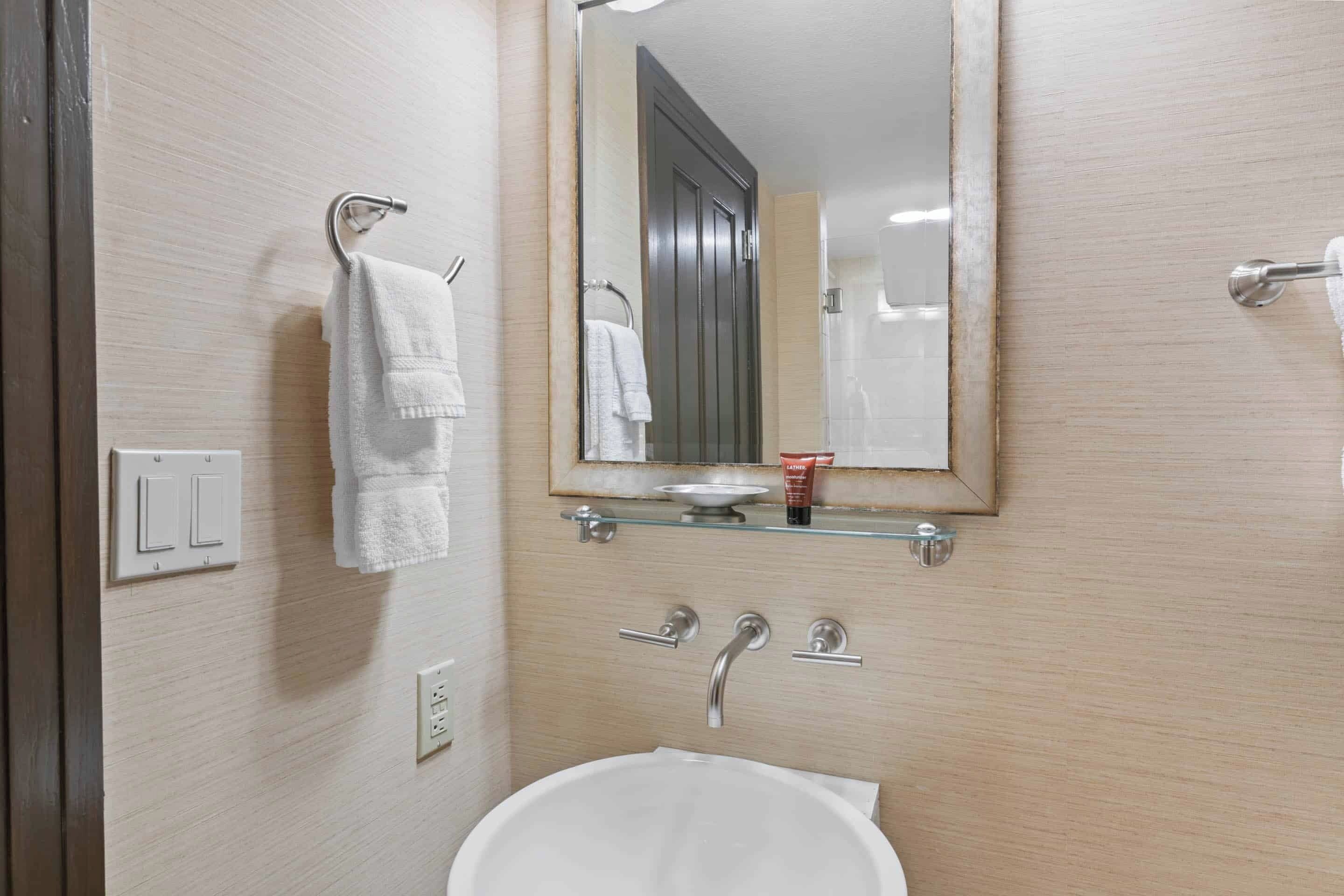 A bathroom with a white sink, a mirror, and two towels hanging on towel bars.