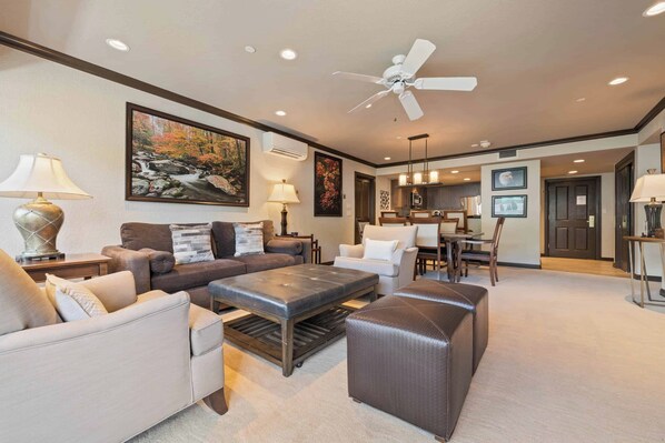 A spacious living room with a ceiling fan, a dining area, and a kitchen in the background.