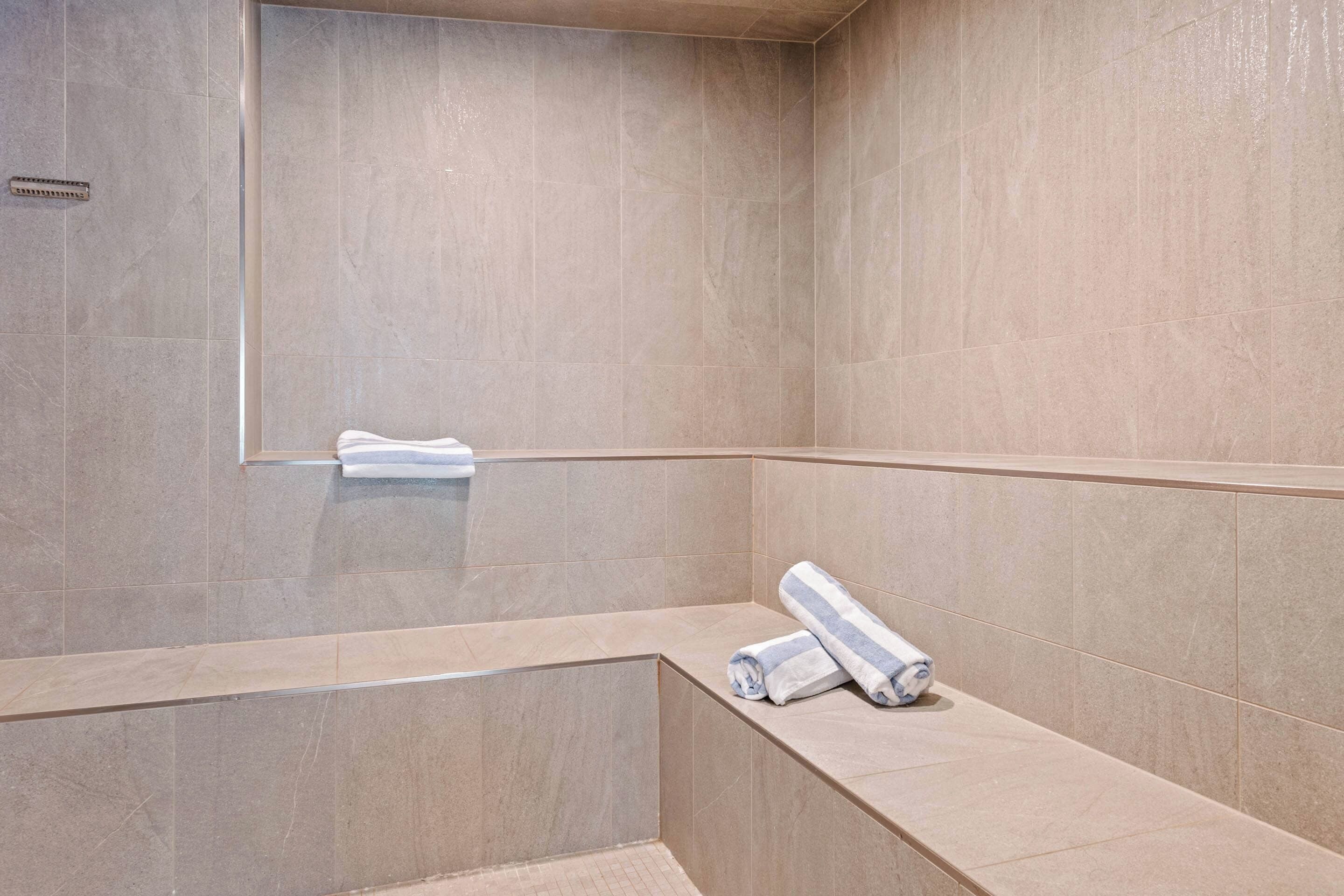 A modern bathroom with beige tiles, a built-in bench, and a towel rack.