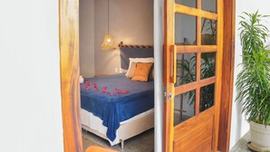 A bedroom with a bed, a bedside lamp, and a wooden door. - Pura Vida Hotel (Itarema)