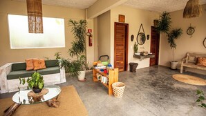 A spacious living area with a green sofa, a glass coffee table, and a bookshelf. There are several potted plants and a wicker basket on the floor. - Pura Vida Hotel (Itarema)