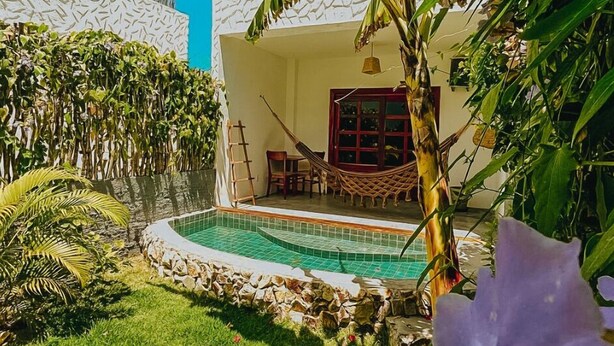 A poolside area with a hammock, a stone wall, and lush greenery. - Pura Vida Hotel (Itarema)