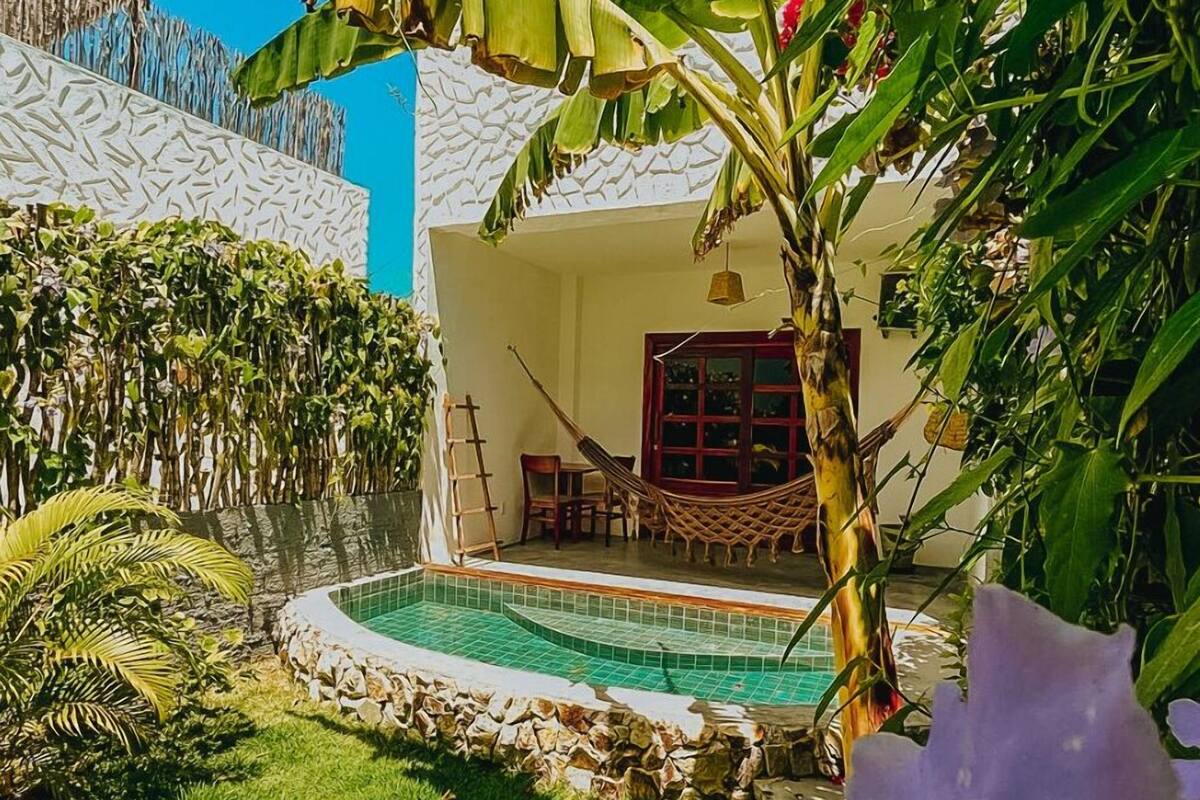 Área de piscina com rede, parede de pedra e vegetação exuberante.