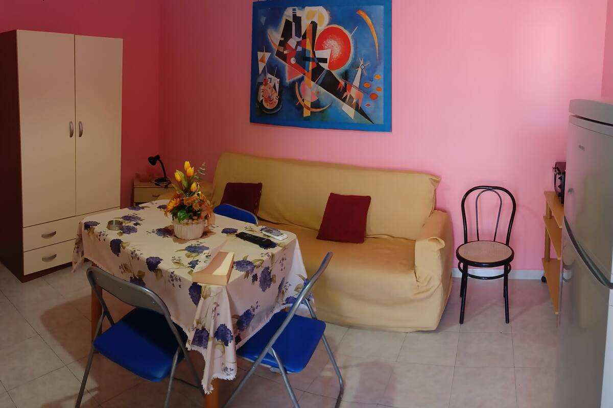 Un espace de vie compact comprenant une table à manger, des chaises, un canapé, un coin cuisine et un grand tableau abstrait accroché au mur.