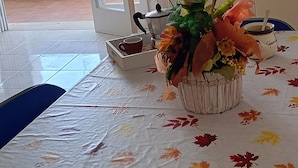 A dining area with a table covered by a tablecloth with a leaf pattern, a floral centerpiece, a coffee pot, and a cup. - Blue Sky Appartamenti San Foca (San Foca)