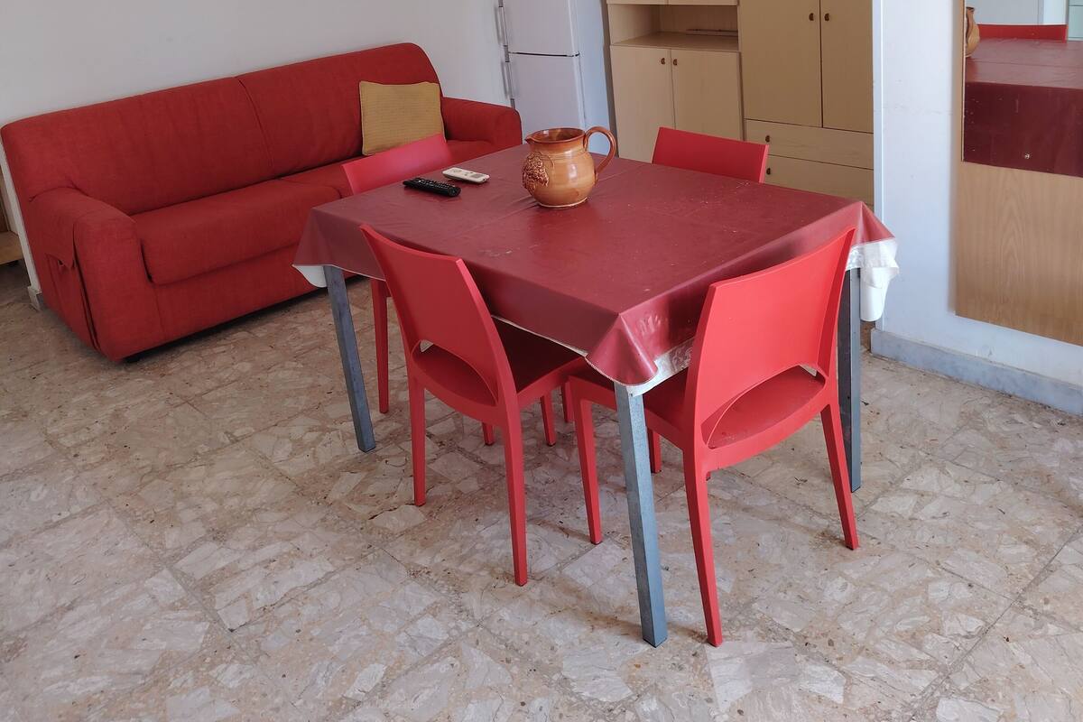 Un espace de vie compact comprenant un canapé rouge, une table à manger avec des chaises, un téléviseur et un réfrigérateur.