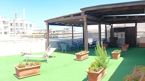 A rooftop terrace with green flooring, several potted plants, a wooden pergola, and outdoor furniture. - Blue Sky Appartamenti San Foca (San Foca)