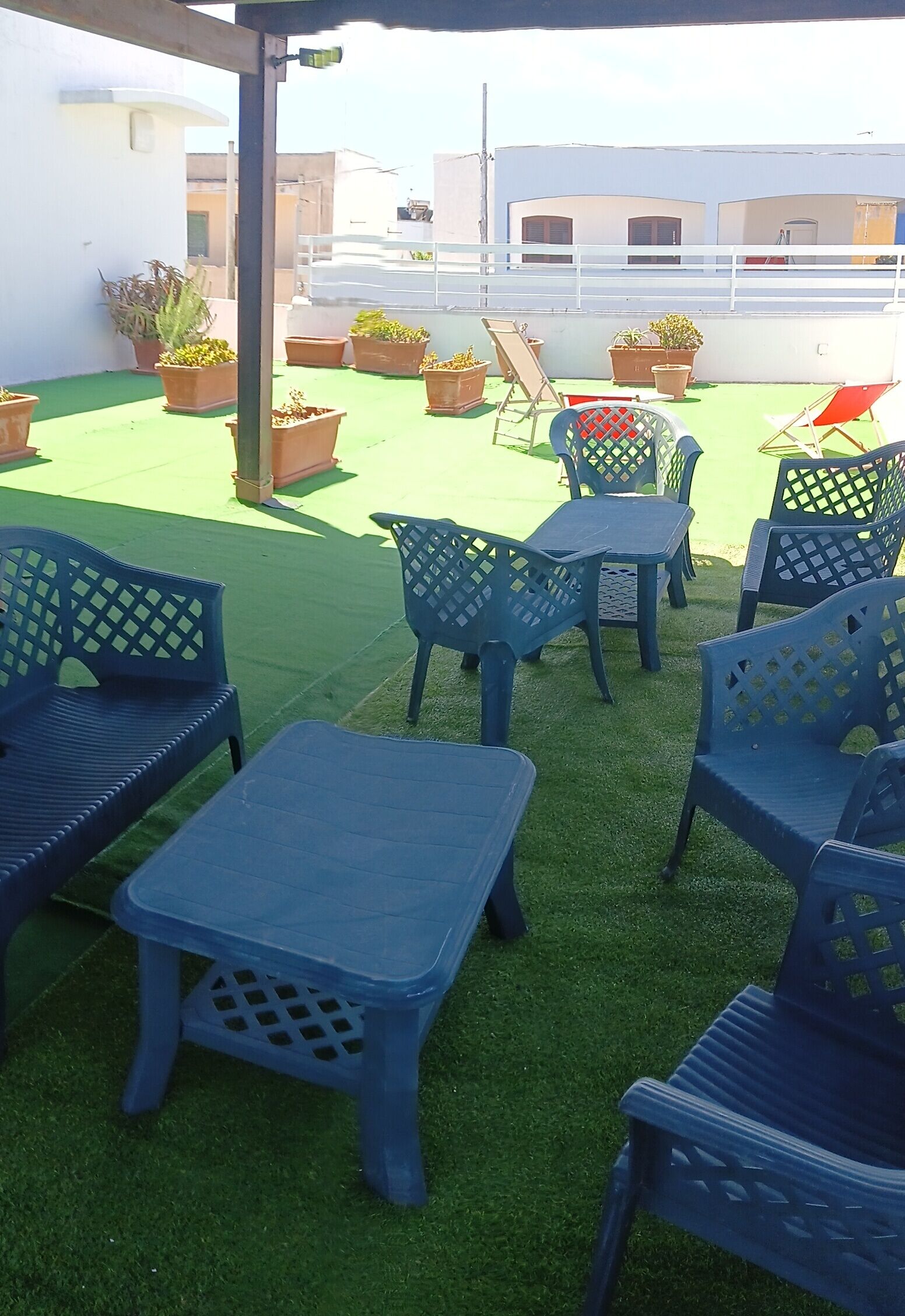 A rooftop patio with blue plastic furniture, green artificial turf, and potted plants.