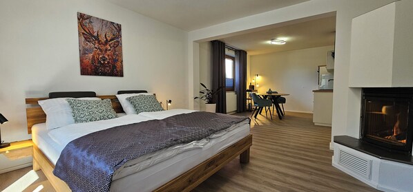 A bedroom with a bed, a painting, a fireplace, and a dining area with a table and chairs.