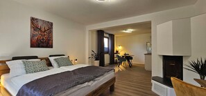 A hotel room with a large bed, a painting on the wall, a dining area with a table and chairs, and a fireplace.