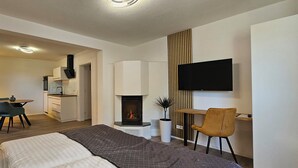 A modern hotel room with a bed, a desk, a chair, a TV, a fireplace, and a dining area with a table and chairs. - ELODIA LUXURY Apartment, WiFi, terrace, kitchen, towels (Heidenheim an der Brenz)