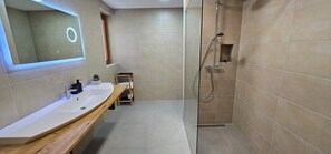 A modern bathroom with a large mirror, a sink, a shower, and a small shelf.