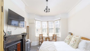 A bedroom with a bed, a fireplace, a television, and a bay window with chairs. - Guest House in Brighton Near Iconic Beach (Brighton)