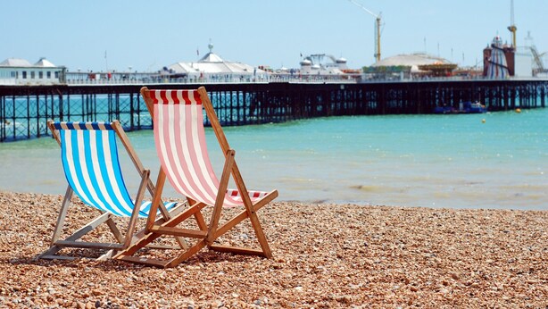 Two beach chairs on a pebbled shore with a pier and buildings in the background. - Guest House in Brighton Near Iconic Beach (Brighton)