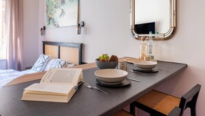 A neatly arranged hotel room with a bed, a bedside table with a book, a bowl of fruit, a bottle, and a mirror. - Modern Apartment in Koblenz Near Mosel River (Koblenz)