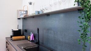 A modern kitchen with a black sink, a countertop, a shelf with wine glasses, and a plant. - Modern Apartment in Koblenz Near Mosel River (Koblenz)