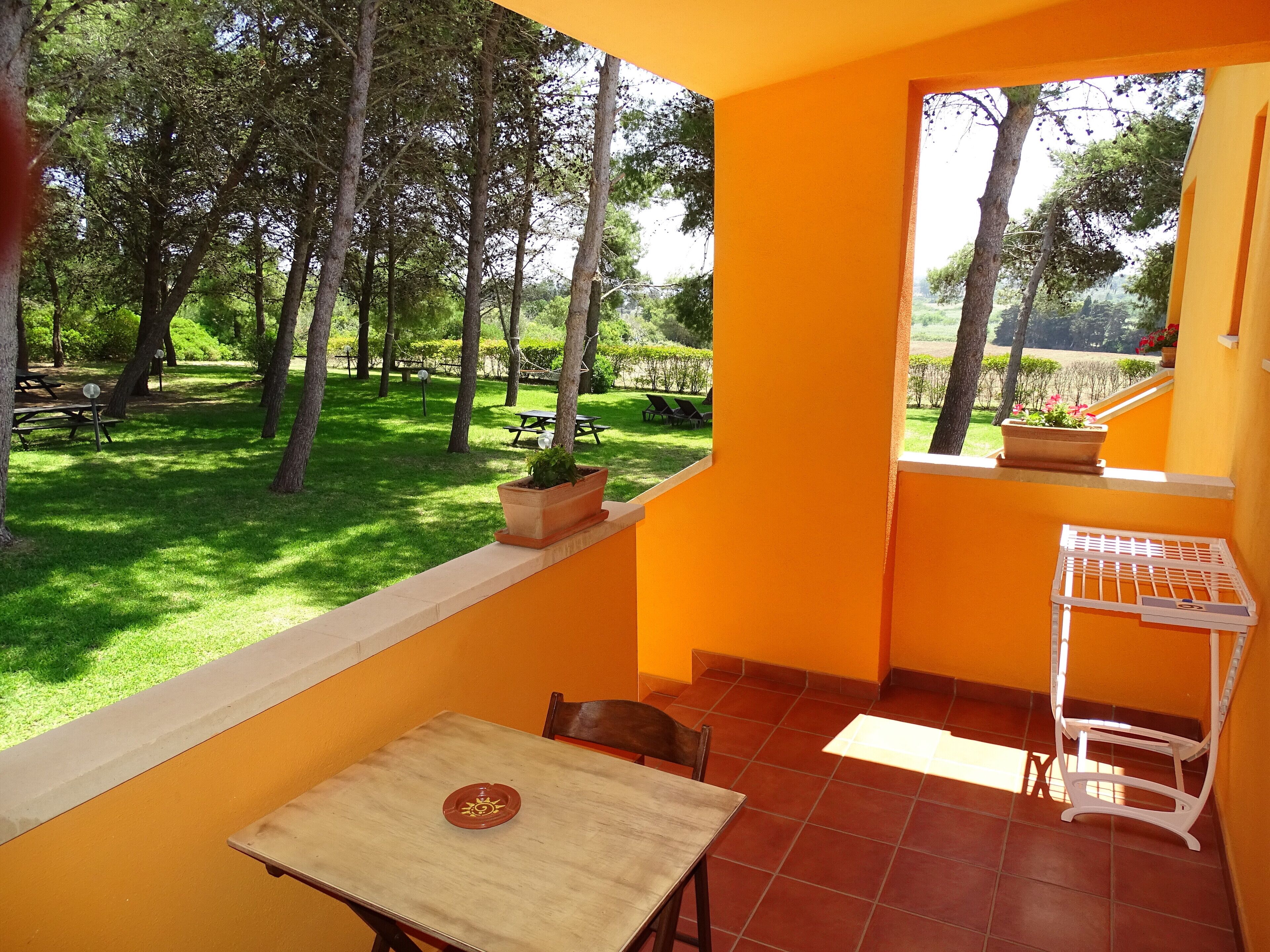A patio with a table and chairs, a small garden view, and a window with a potted plant.