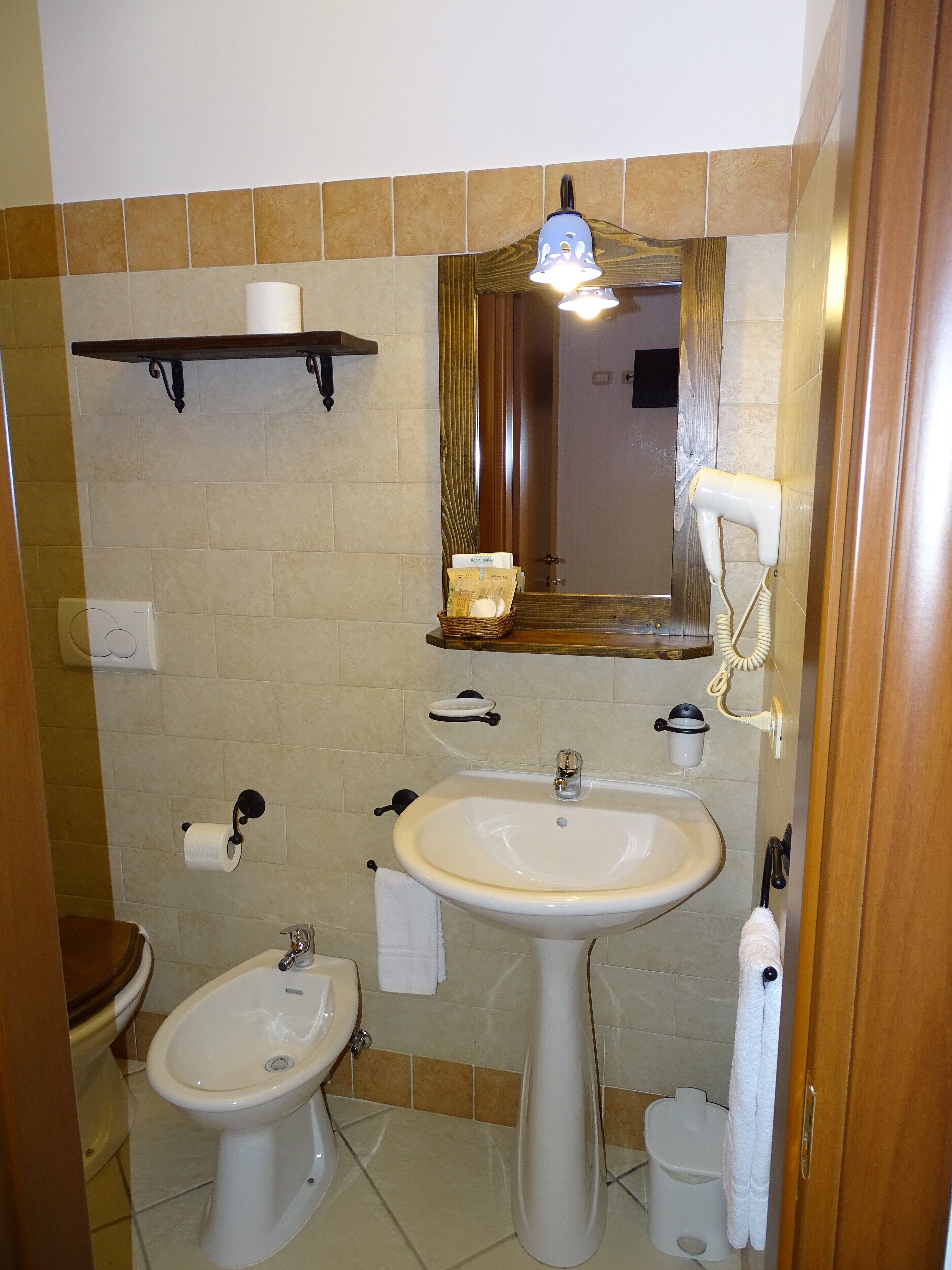 A bathroom with a sink, bidet, toilet, towel rack, and a mirror with a light fixture.