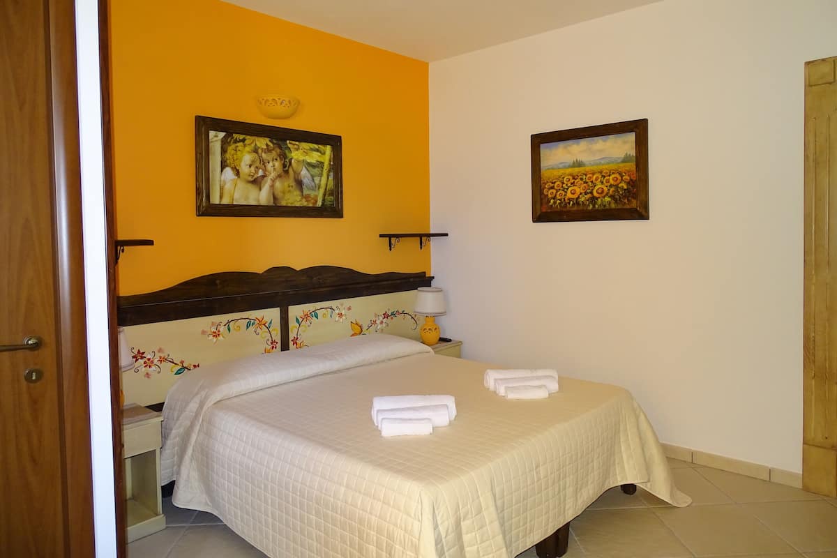 A bedroom with a bed, a nightstand, a lamp, and two framed pictures on the wall.