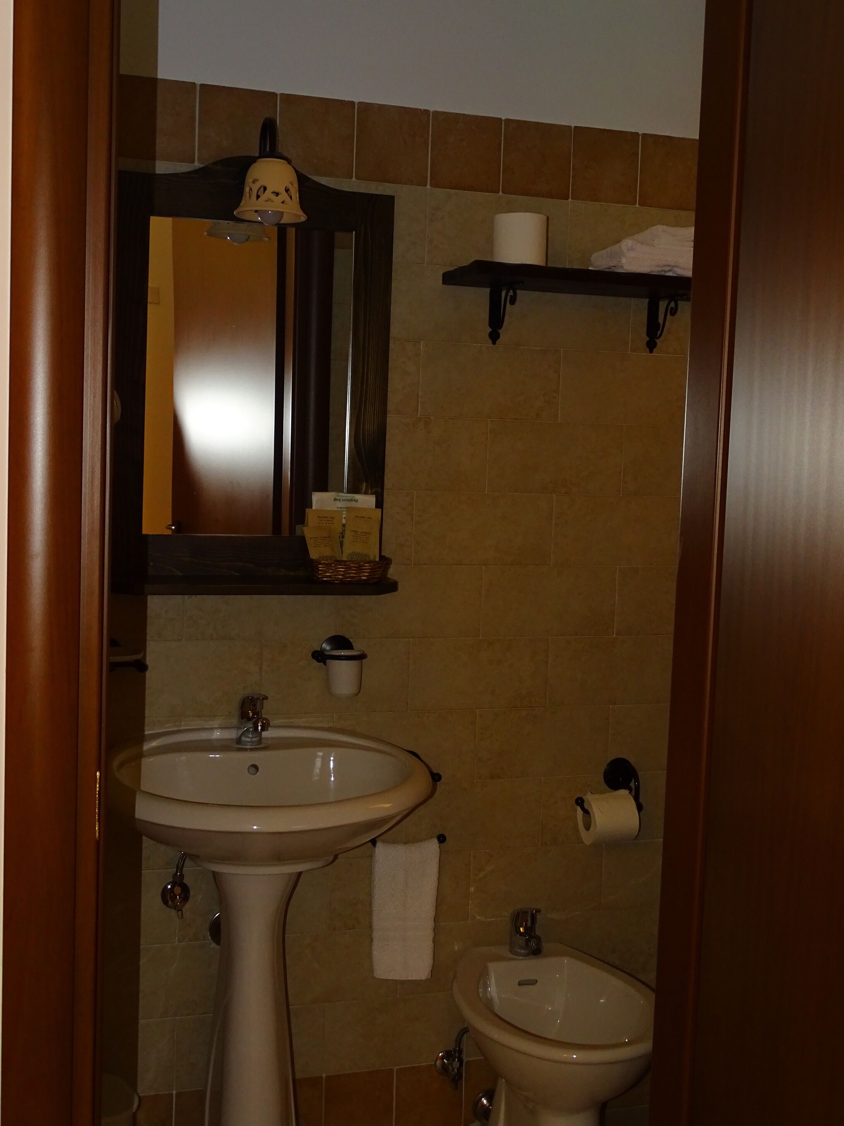 Une salle de bain comprenant un lavabo sur colonne, un petit lavabo, un miroir, un porte-serviettes et une étagère avec des articles de toilette.