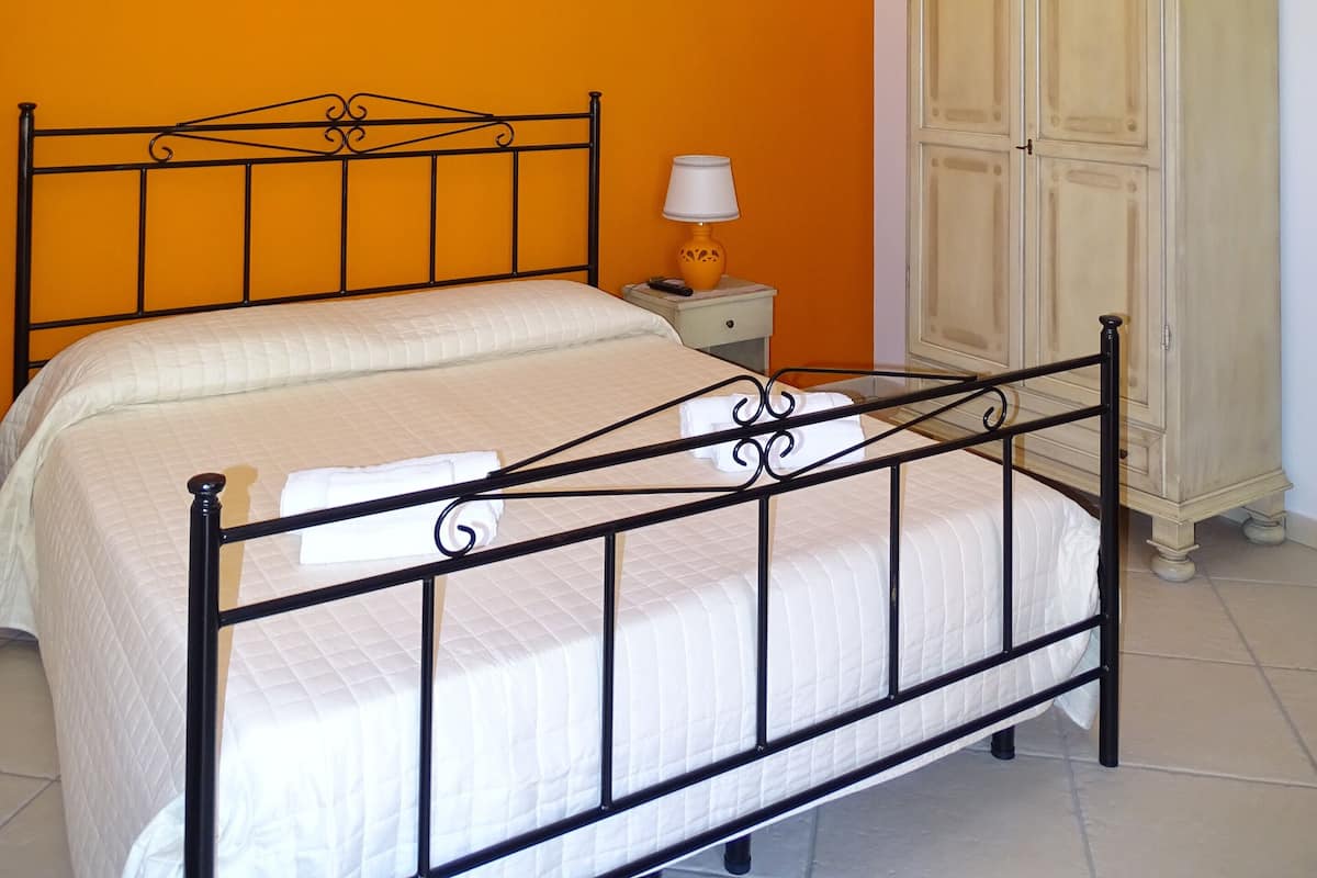 A bedroom with a bed, a nightstand, a lamp, a wardrobe, and a wall painting.