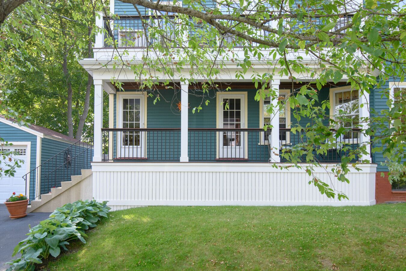 Een tweelaags huis met een veranda, witte details en een groene gevel.