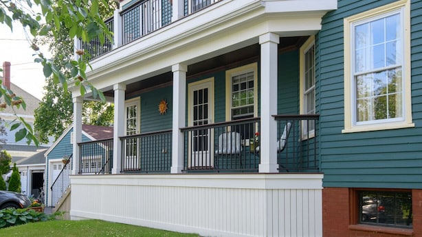A two-story house with a covered front porch and a brick foundation. - Luxury on Back Cove - Three Gables (Portland)