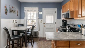 A kitchen with wooden cabinets, a stove, and a dining area with a table and chairs. - Luxury on Back Cove - Three Gables (Portland)