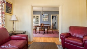 A living room with red leather sofas, a wooden coffee table, a dining table with chairs, and a chandelier. - Luxury on Back Cove - Three Gables (Portland)