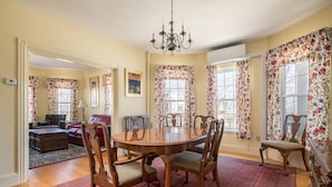 A dining area with a round wooden table surrounded by six chairs, a chandelier, and floral curtains. - Luxury on Back Cove - Three Gables (Portland)