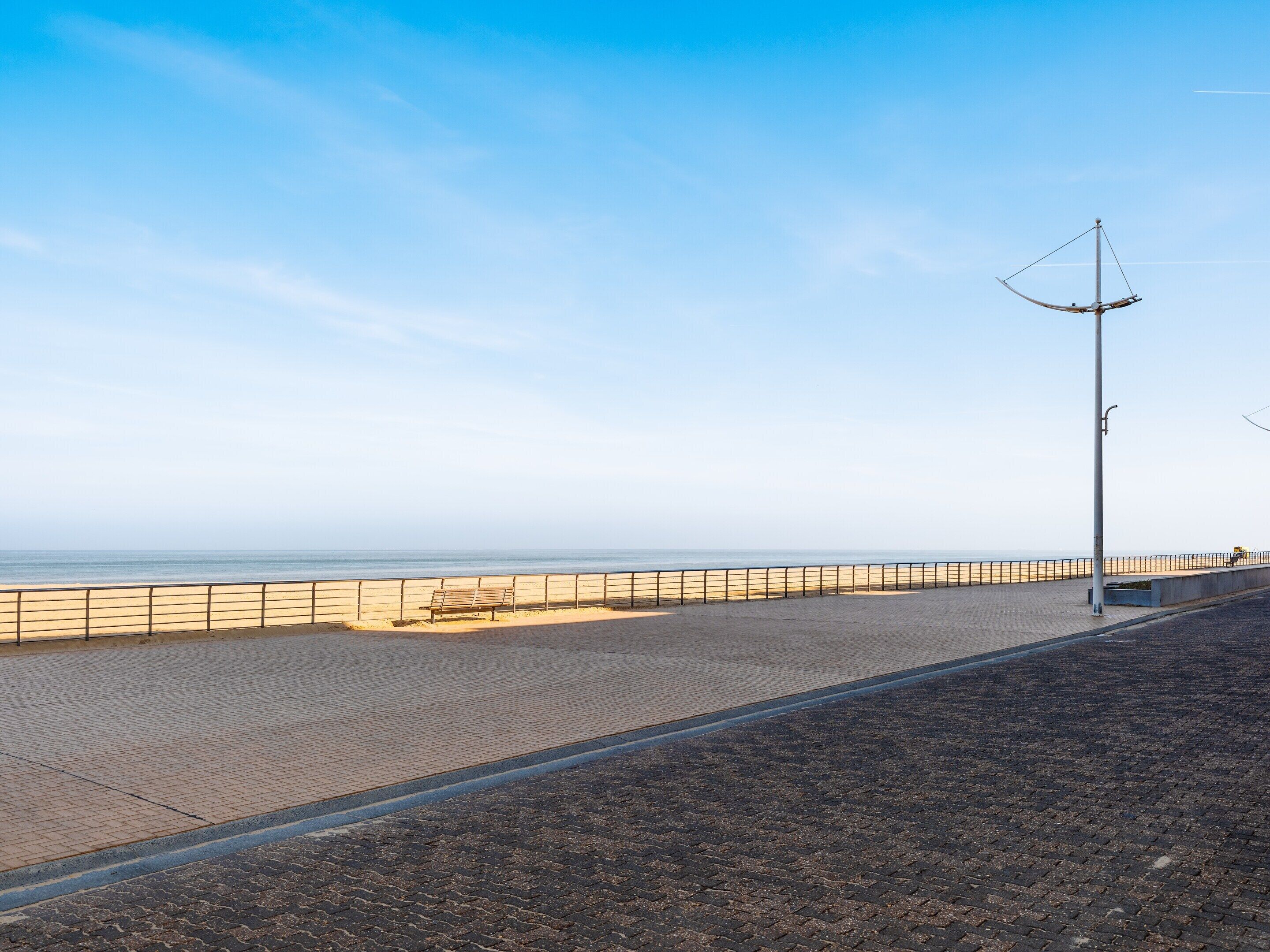A paved walkway along a beach with a metal fence and a bench.