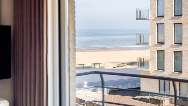 Une vue depuis une fenêtre donnant sur une plage, avec un bâtiment au premier plan.