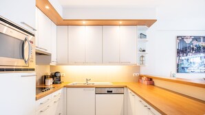 Une cuisine moderne avec des armoires blanches, un plan de travail en bois, un four à micro-ondes encastré, une machine à café et un lave-vaisselle.