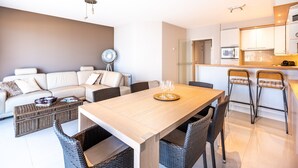 Un salon moderne comprenant un canapé, une table à manger avec des chaises, un ventilateur et un coin cuisine avec un four à micro-ondes.