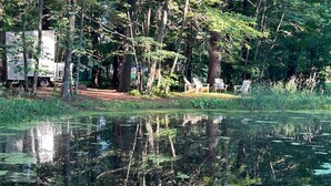 Un terrain de camping avec une tente et une caravane, entouré d’arbres et bordé d’un étang.