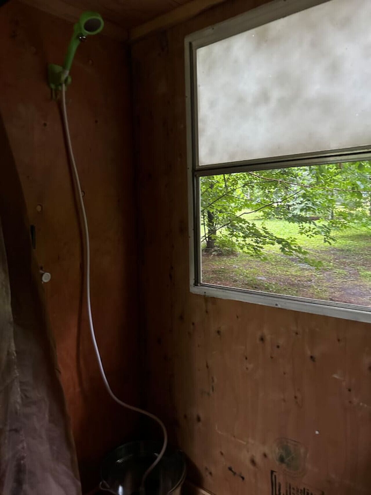 Una habitación de madera con una ventana, una manguera verde y un balde de metal.