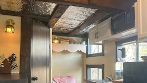 Een kleine keuken met een magnetron, gootsteen en een slaapgedeelte met een bed en kussens.