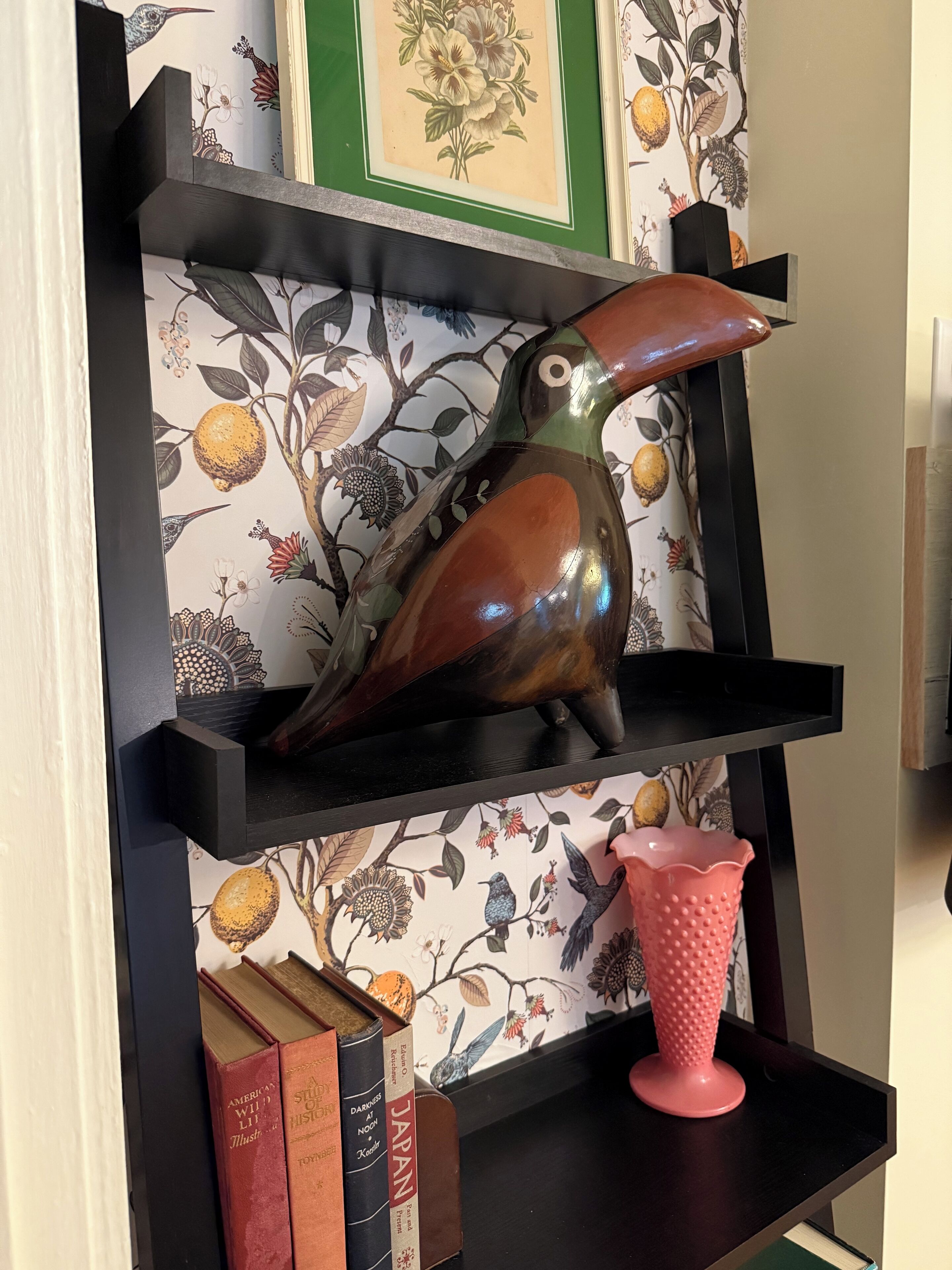 A bookshelf with a decorative bird sculpture, a pink textured vase, and books.