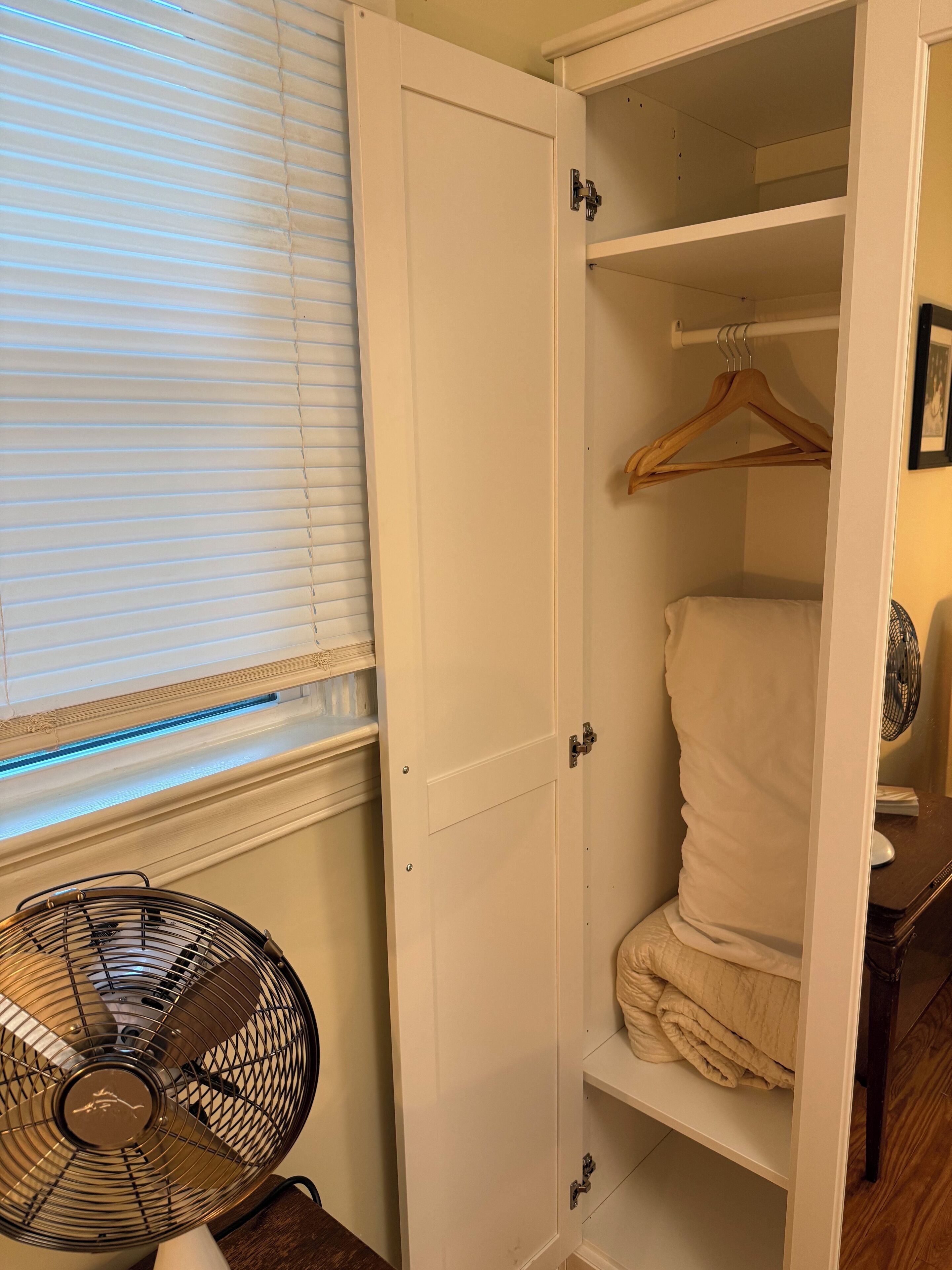 A walk-in closet with a hanging rod, a fan, and a window with blinds.