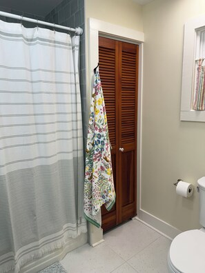 A bathroom with a shower curtain, a wooden door, a toilet, and a towel hanging on the door.