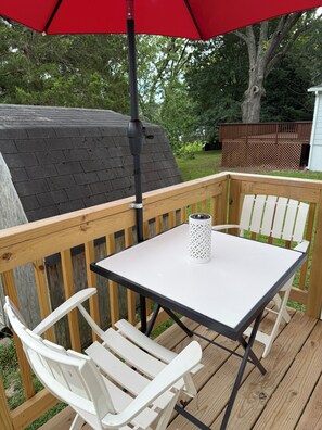 A wooden deck with a white table and chairs, a red umbrella, and a white lantern.