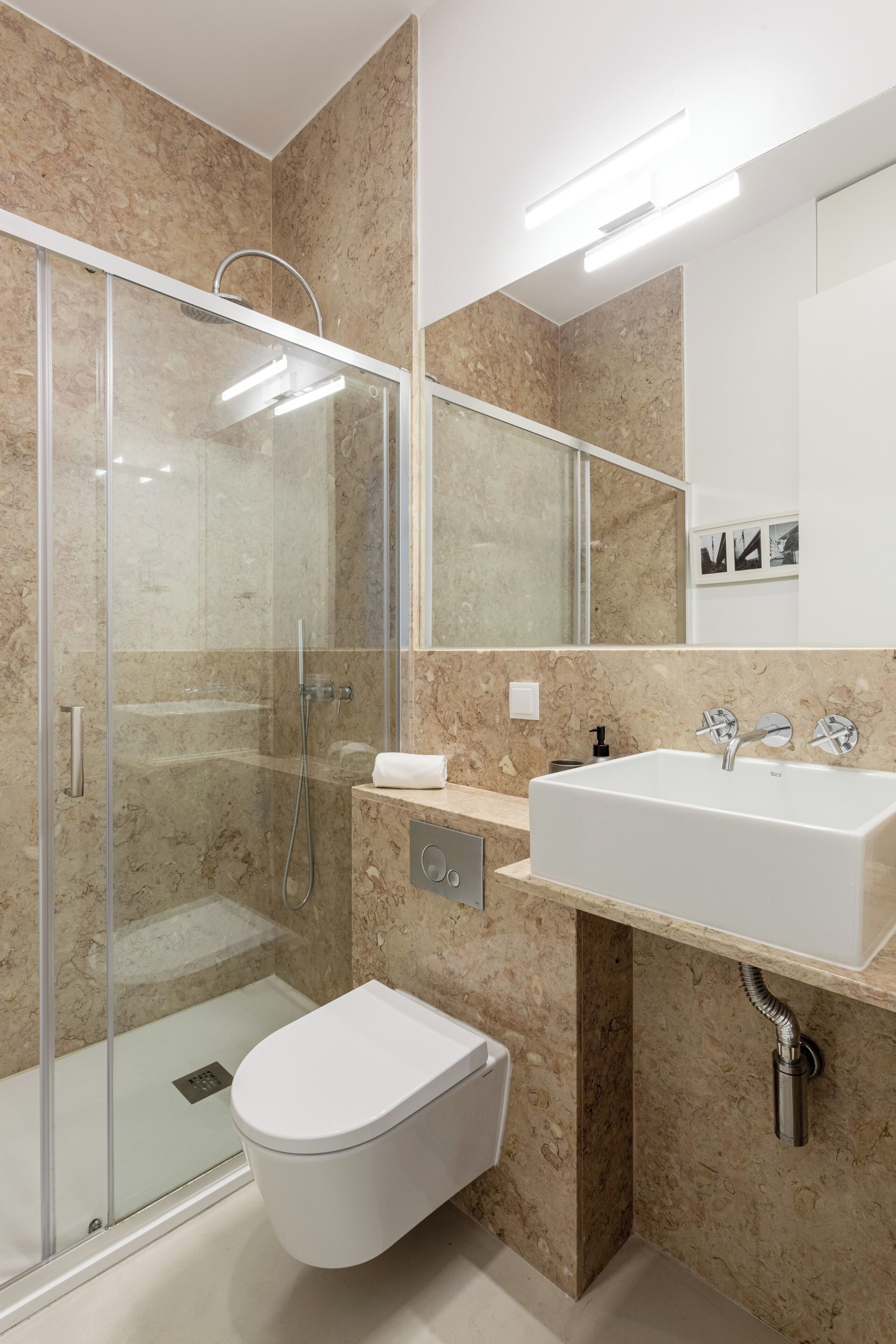 Un baño moderno con ducha de vidrio, un lavamanos blanco y un inodoro.