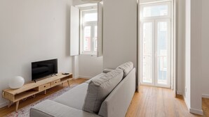 Un salon moderne avec un canapé, un téléviseur posé sur un meuble en bois et une grande fenêtre.