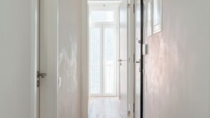 Un couloir doté d’un plancher en bois, de murs blancs et de portes donnant sur une pièce lumineuse.