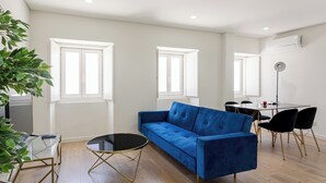 A modern living room with a blue sofa, a glass coffee table, and a dining area with a table and chairs.