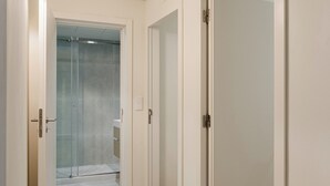 A hallway with white walls and doors leading to a bathroom with a glass shower.