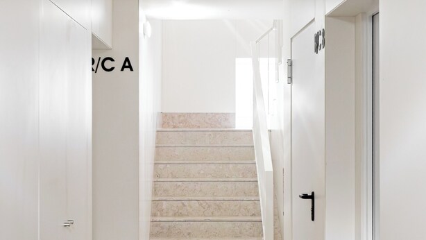 A hallway with a marble floor, white walls, and a staircase leading to another floor.